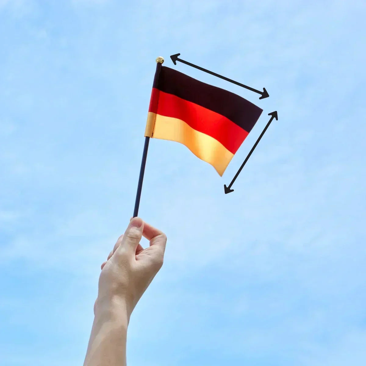 Eine Hand hält eine kleine Deutschlandfahne vor blauem Himmel, ergänzt durch Pfeile zur Darstellung der Flaggenmaße.